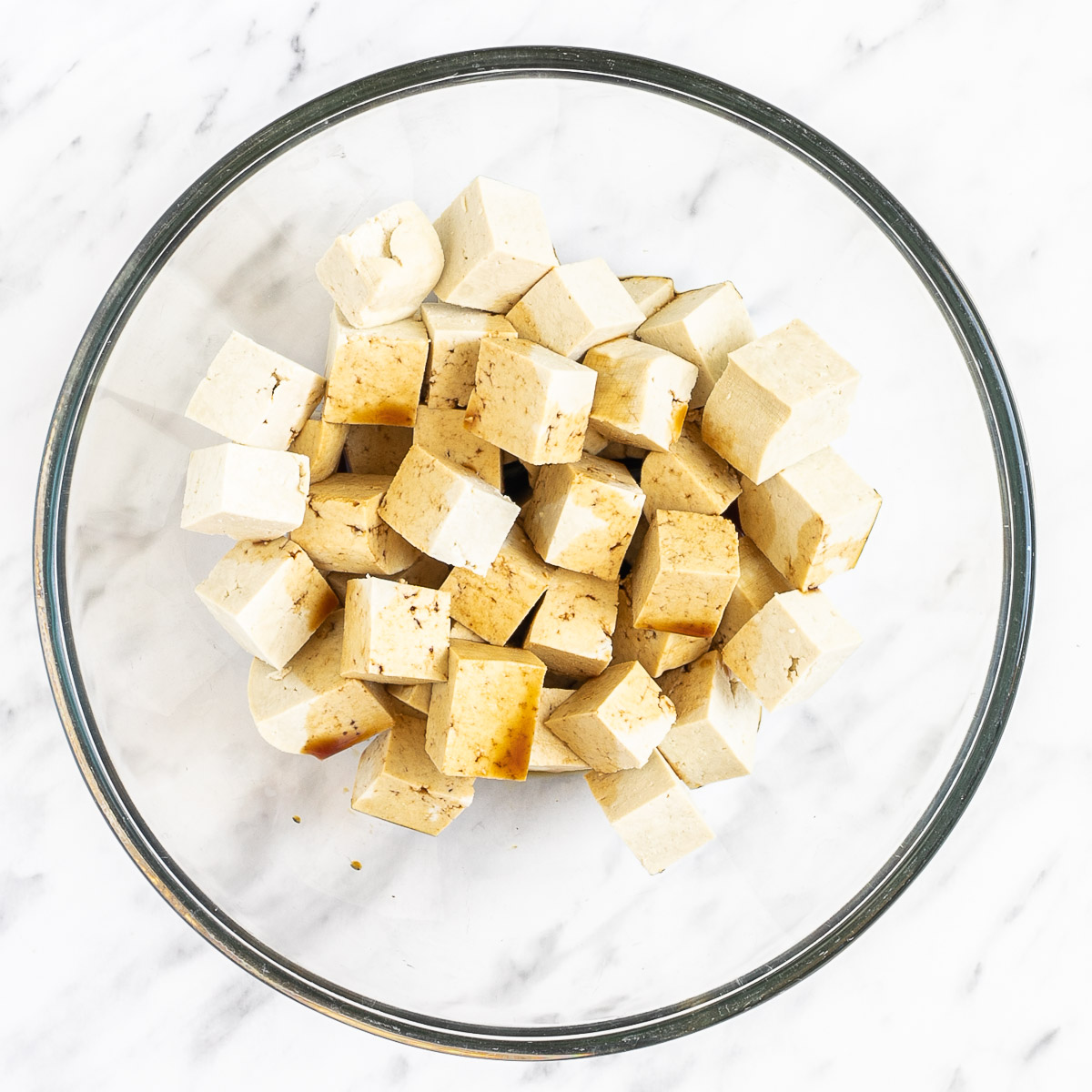 Tofu cubes in a bowl drizzled with dark sauce.