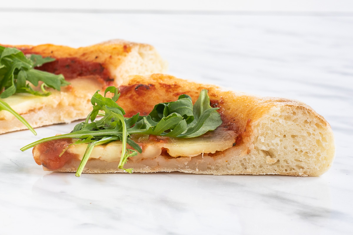 Slice of pizza with tomato sauce and arugula from the side to see the airy fluffy crust