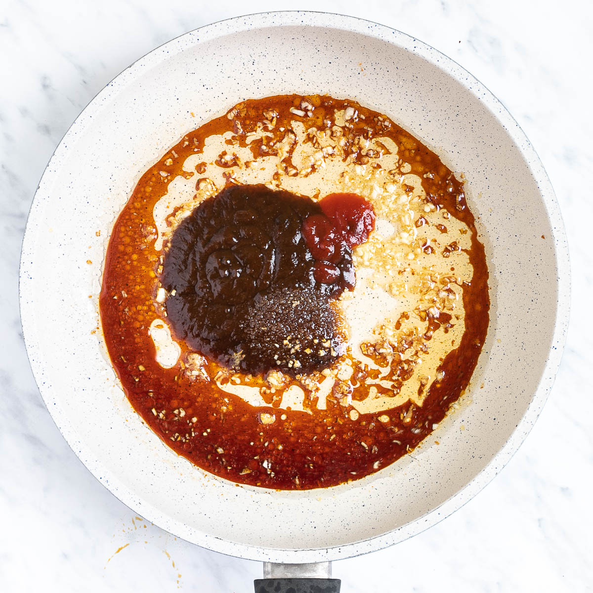 A white frying pan with different dark liquids and spices.