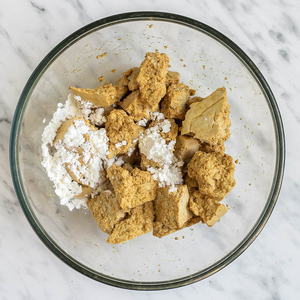 Light brown torn tofu pieces with a heap of white powder in a glass bowl. 