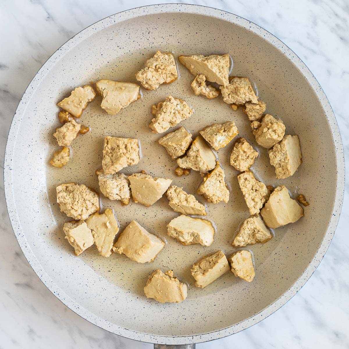Light brown torn tofu pieces in a white frying pan.