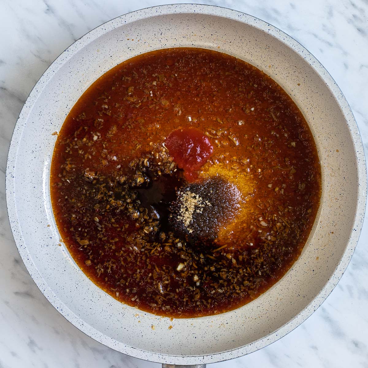 A white frying pan with different dark liquids and spices.