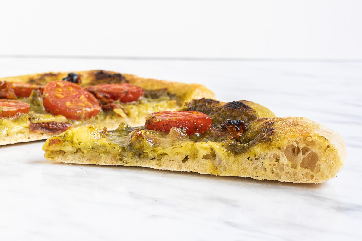 Slice of pizza with pesto sauce and tomato from the side to see the airy fluffy crust