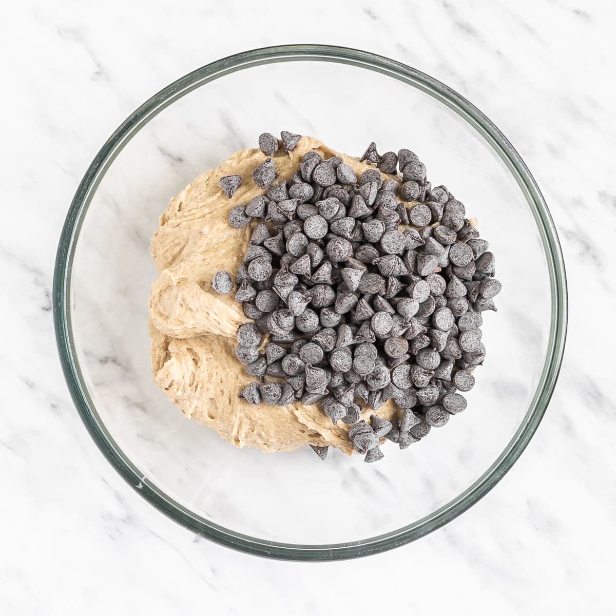 Glass bowl with light brown creamy batter topped with lots of chocolate chips.