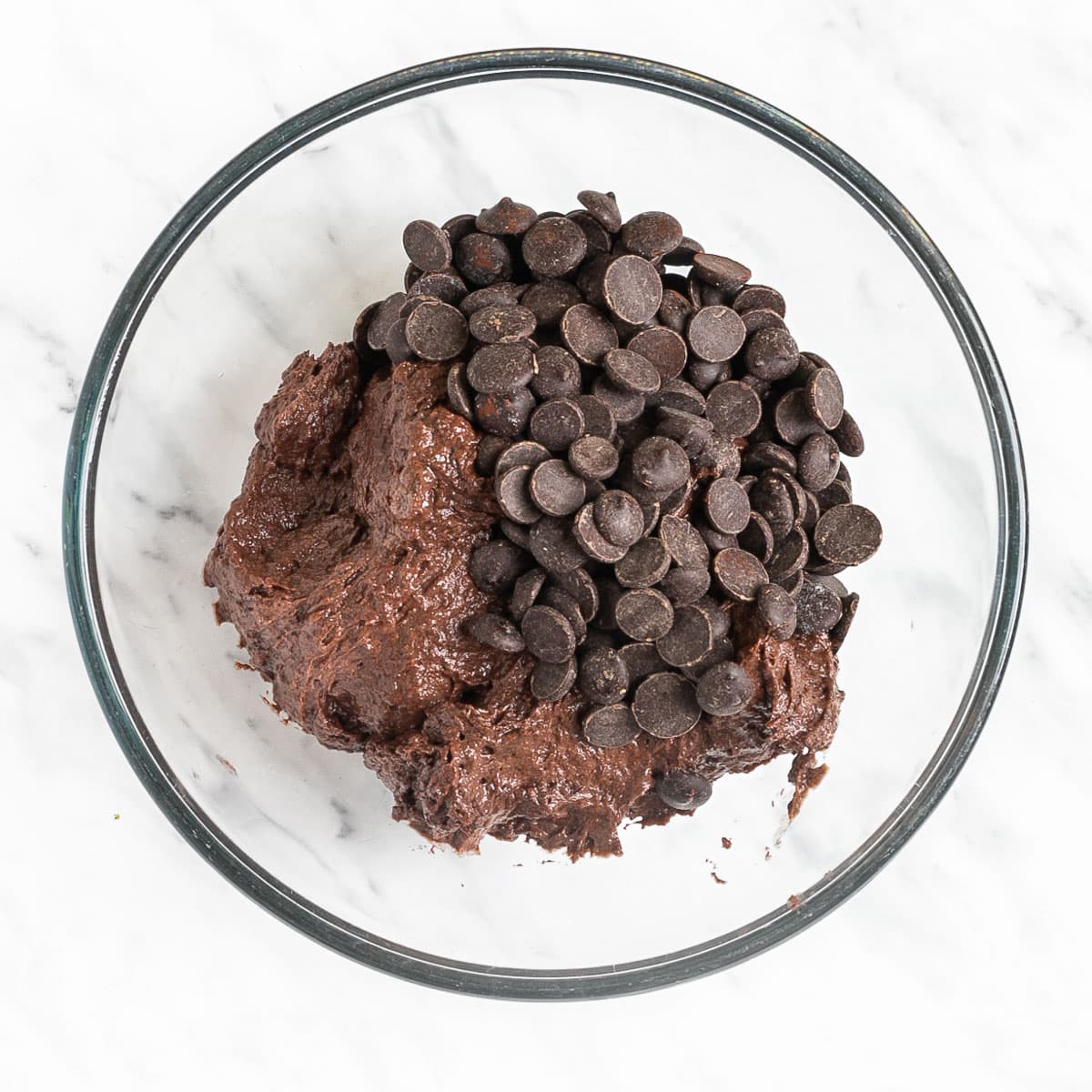 Glass bowl with dark brown creamy batter topped with lots of chocolate chips