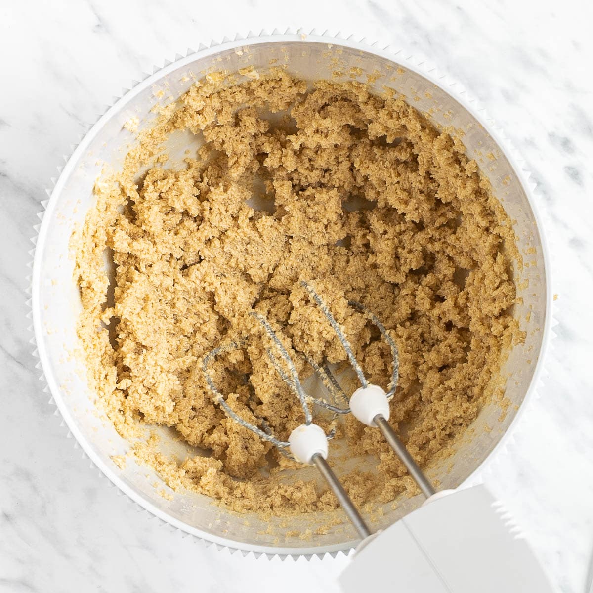 A white bowl with a hand blender and soft light brown batter.
