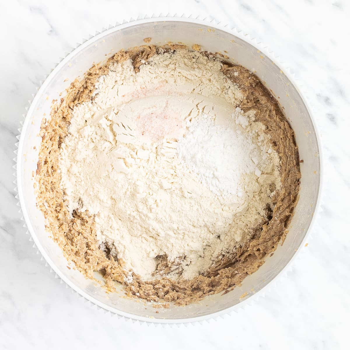 Soft light brown batter and a heap of flour in a white bowl.