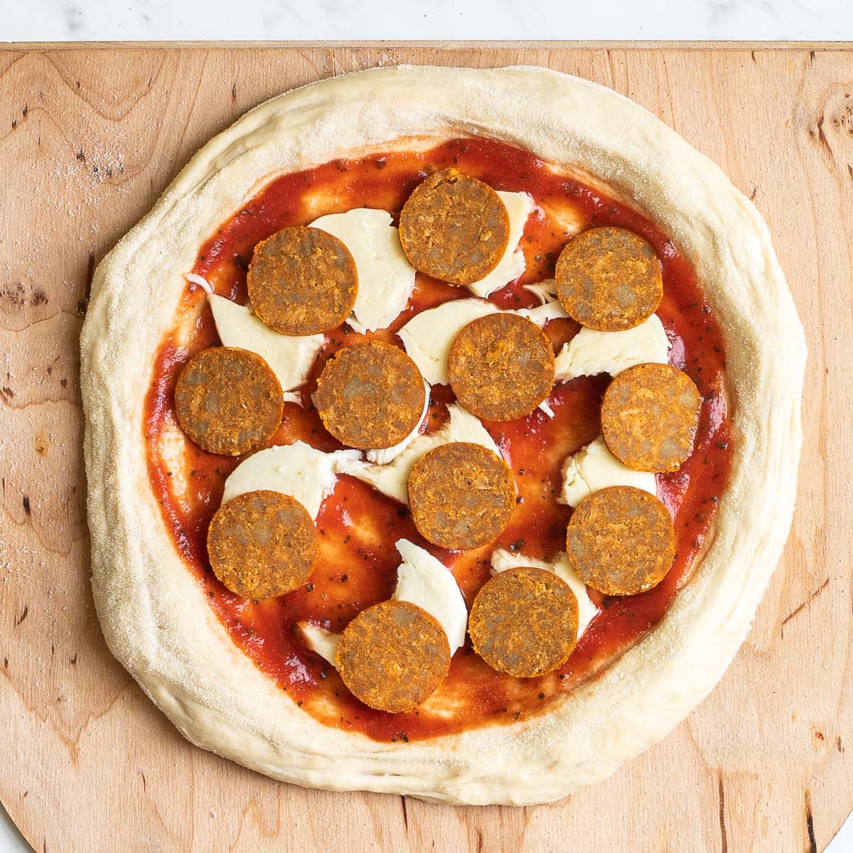 Unbaked pizza on a wooden baker's peel topped with tomato sauce, cheese and pepperoni slices.