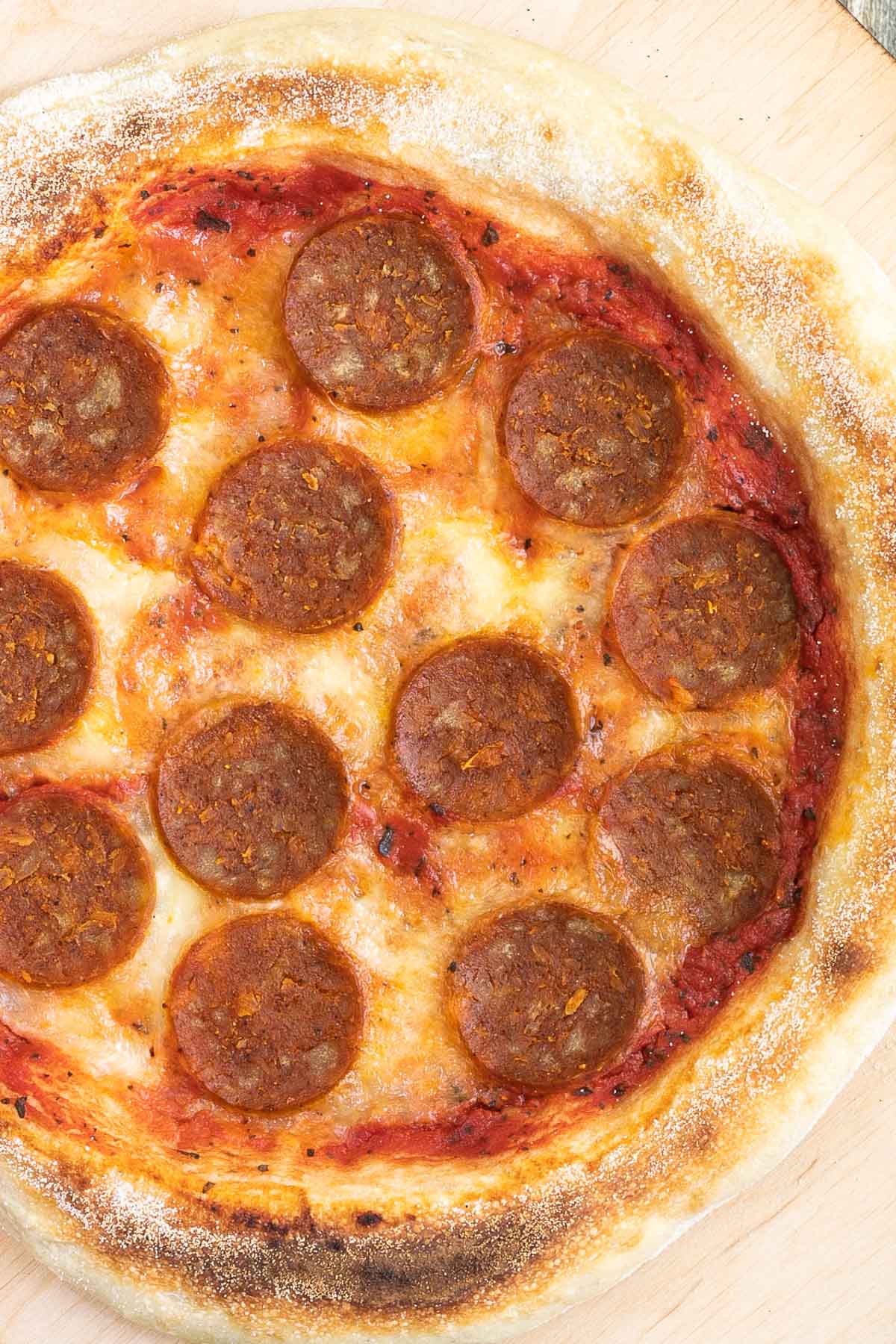 Pizza on a wooden baker's peel topped with tomato sauce, melted cheese and pepperoni slices.