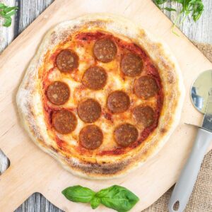 Pizza on a wooden baker's peel topped with tomato sauce, melted cheese and pepperoni slices.