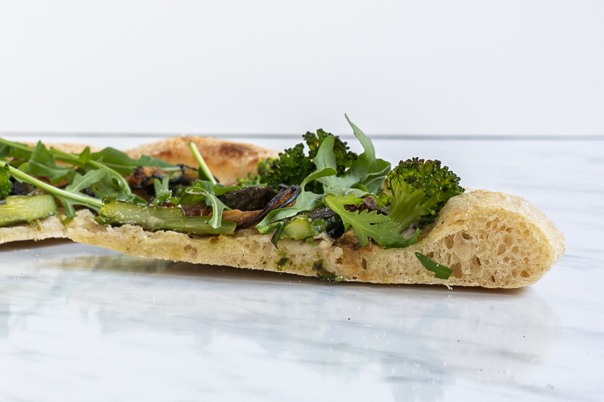 A slice of pizza with green toppings from the side.