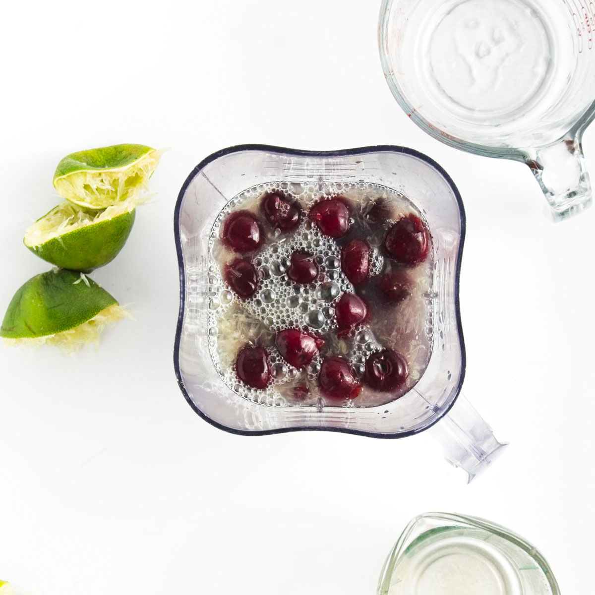 A blender with liquid and cherries.