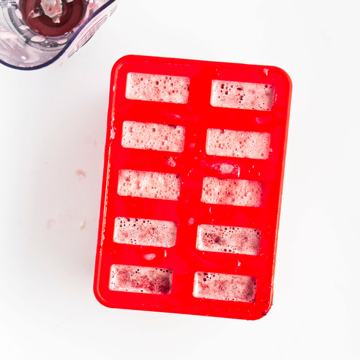 Red popsicle mold with 10 holes filled to the brim with pink liquid.