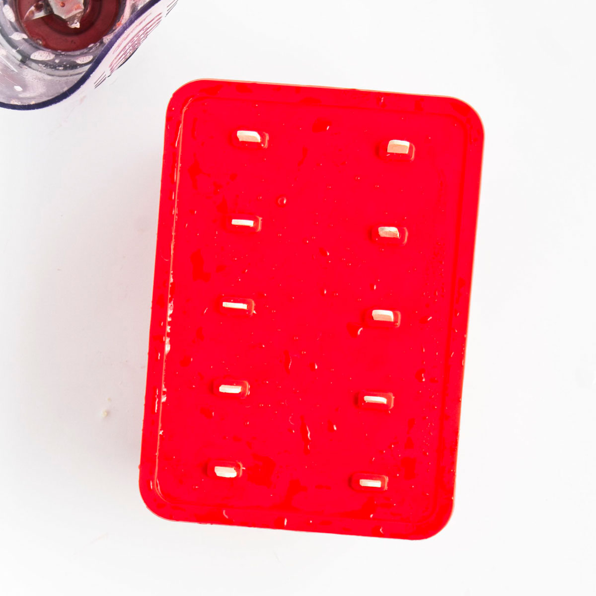 Red popsicle mold with the cover top on and 10 sticks are sticking out from it.