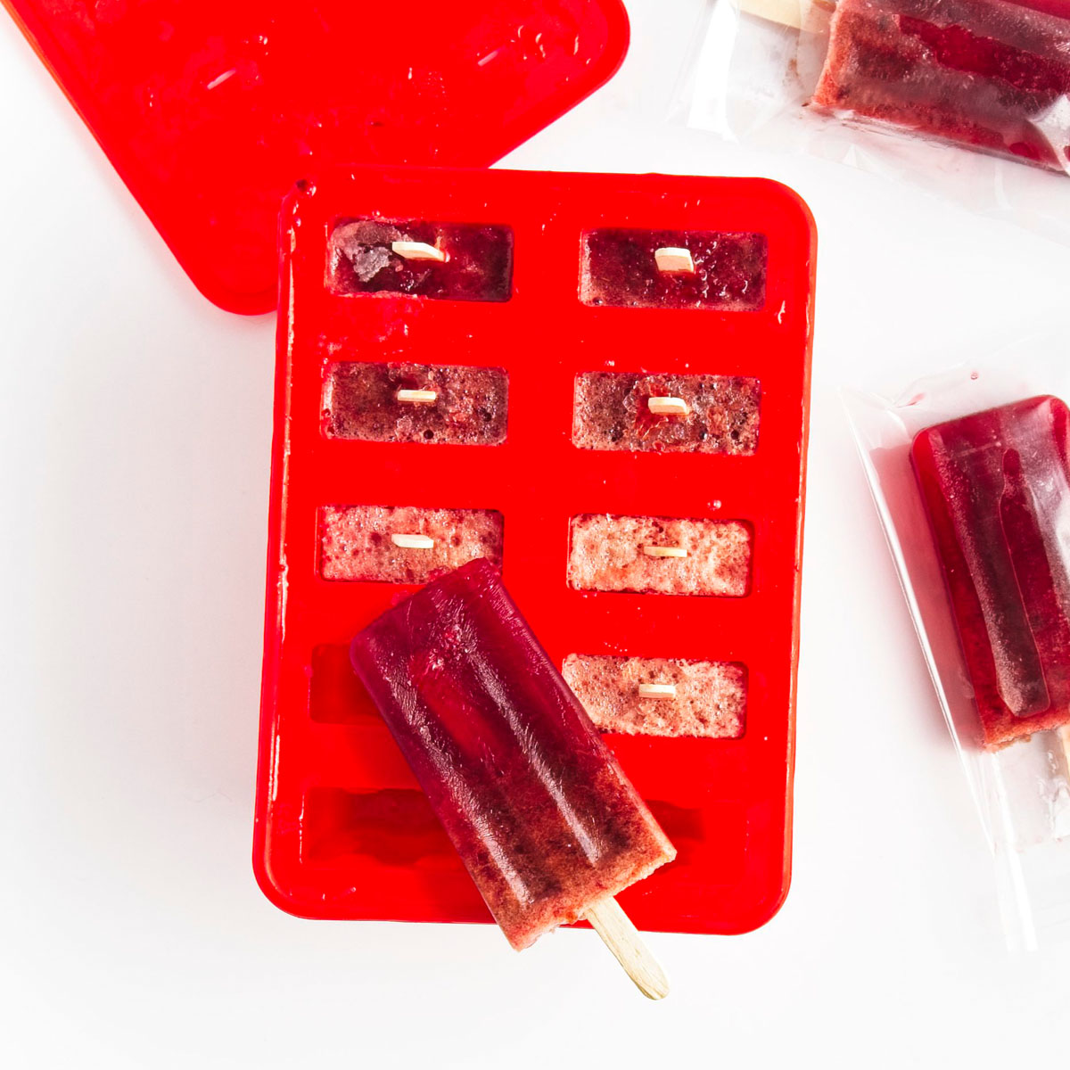 Vibrant purple popsicles in a red mold. Two has been removed and placed one on top and one on the side.