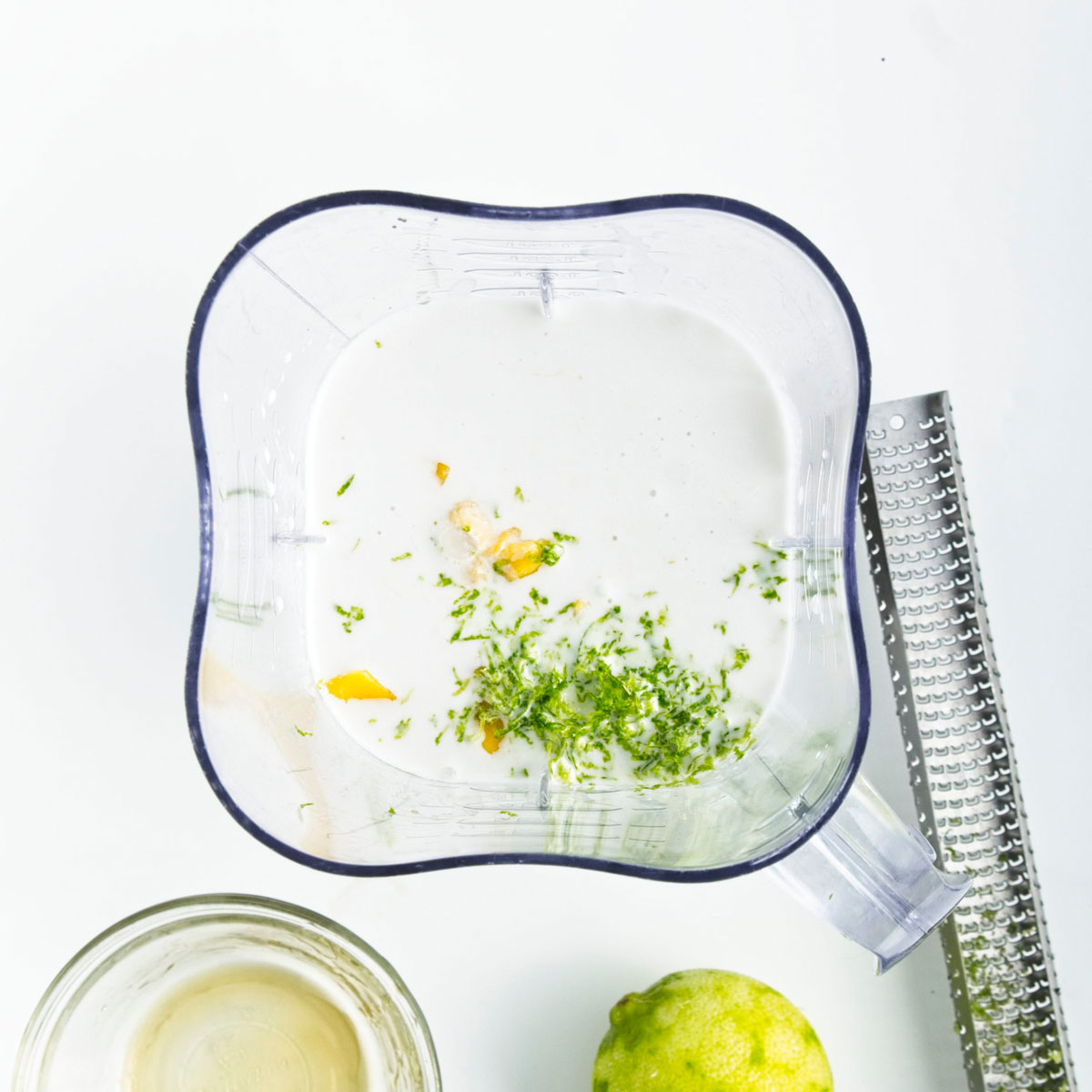Blender with white liquid, yellow mango pieces and green lime zest.