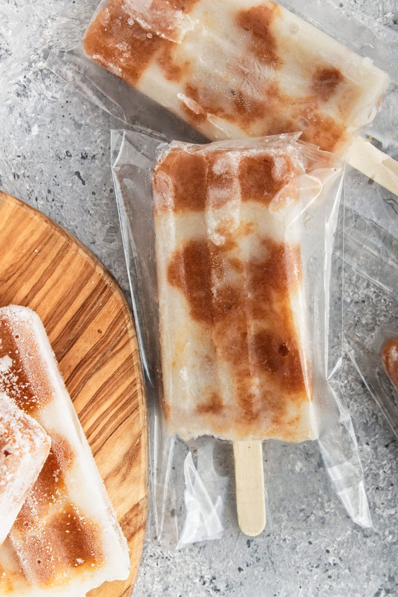 Brown and white popsicles wrapped in a plastic wrap on a grey surface.