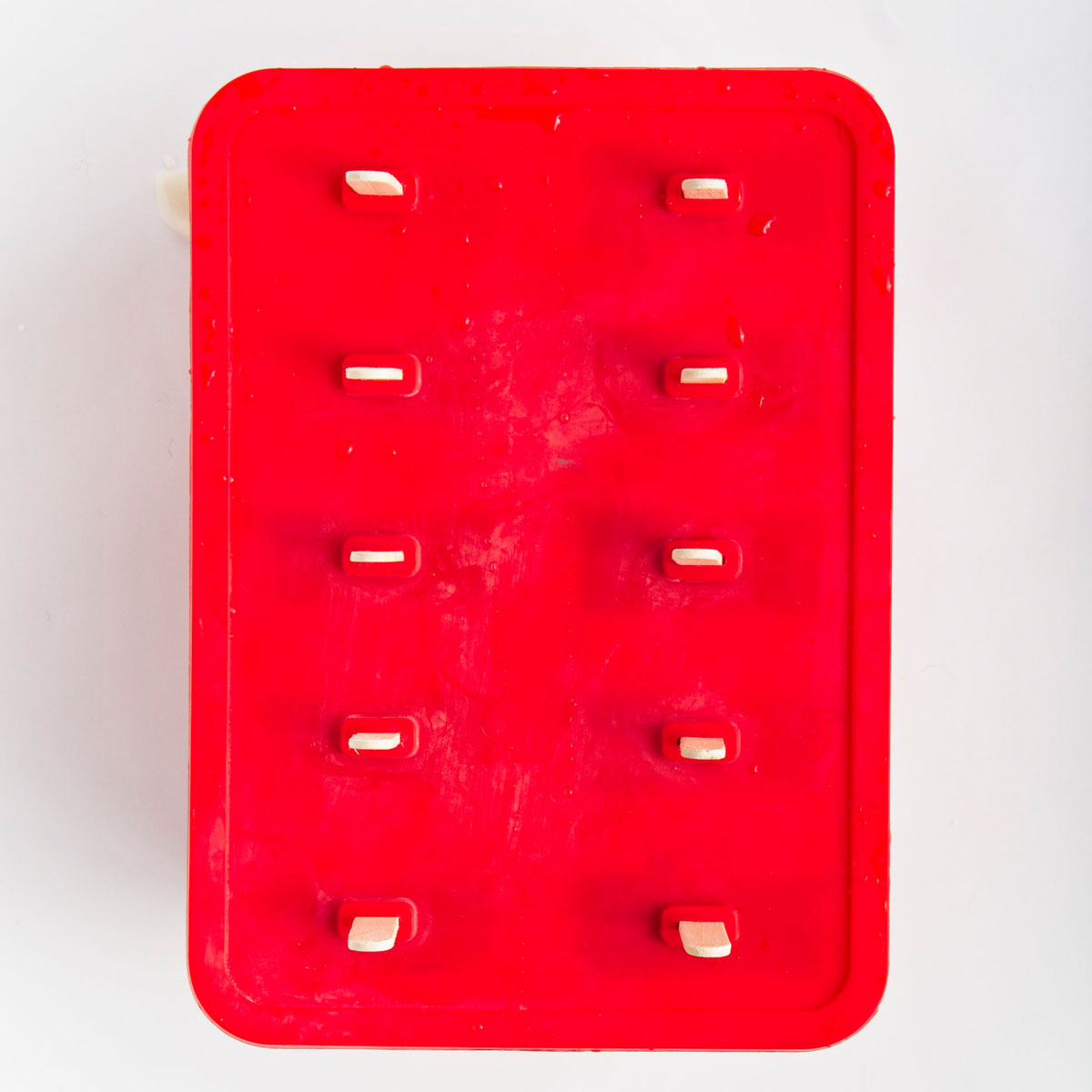 Red popsicle mold with the cover top on and 10 sticks are sticking out from it.
