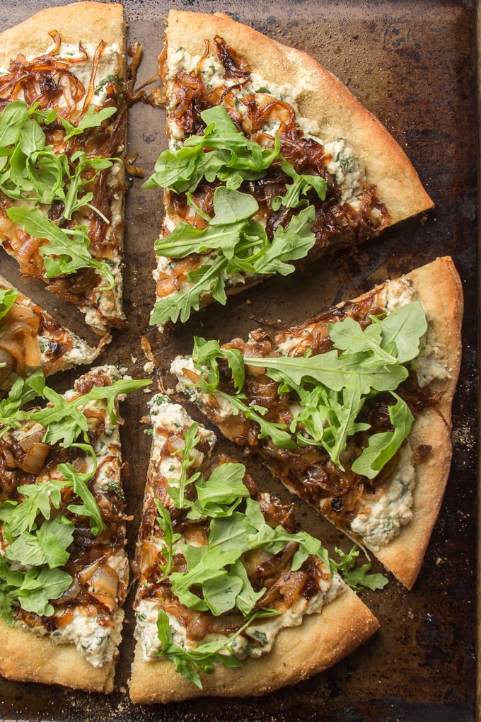 Pizza with cream cheese-like herby sauce, dark brown caramelized onion, and arugula.