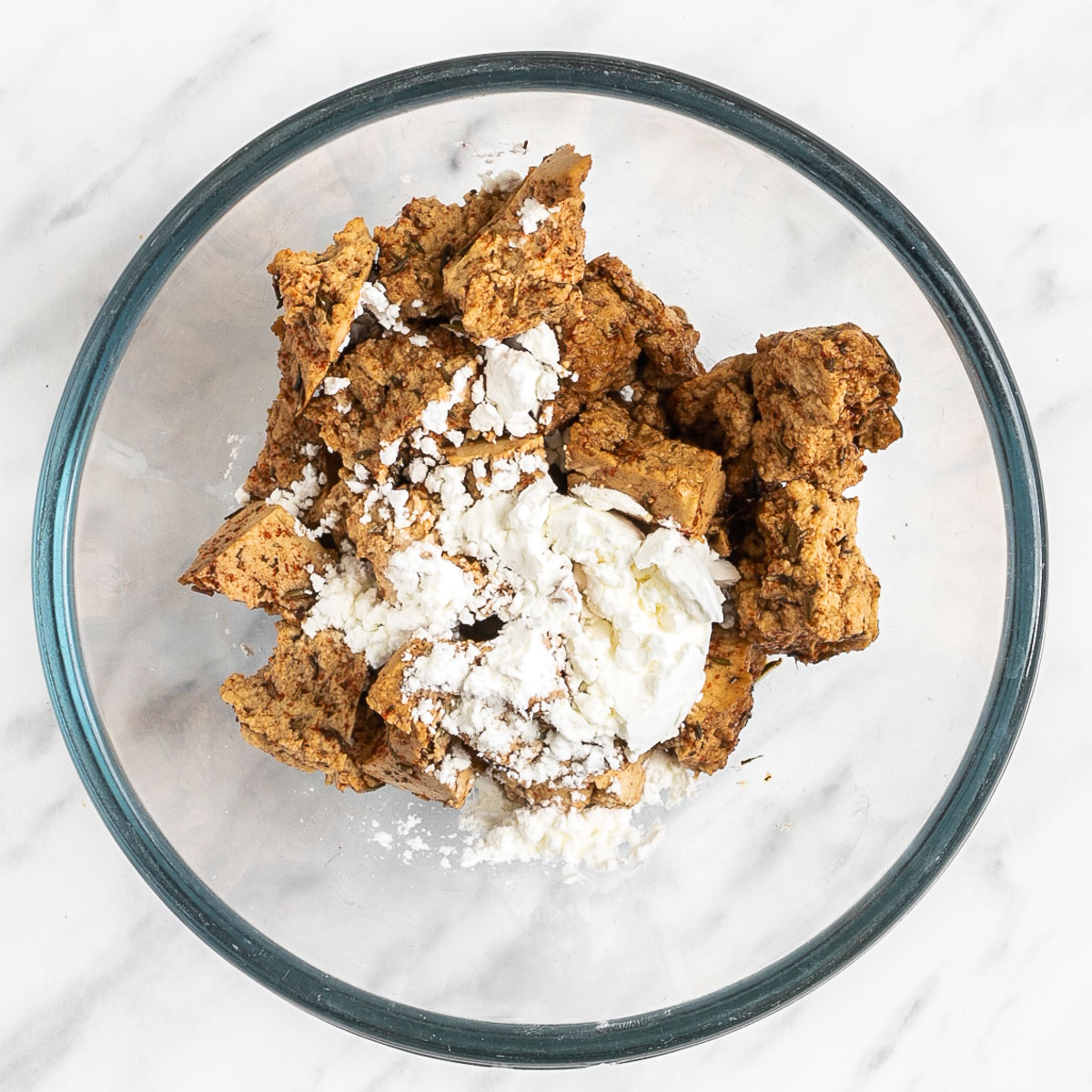 Light brown torn tofu pieces with a heap of white powder in a glass bowl.