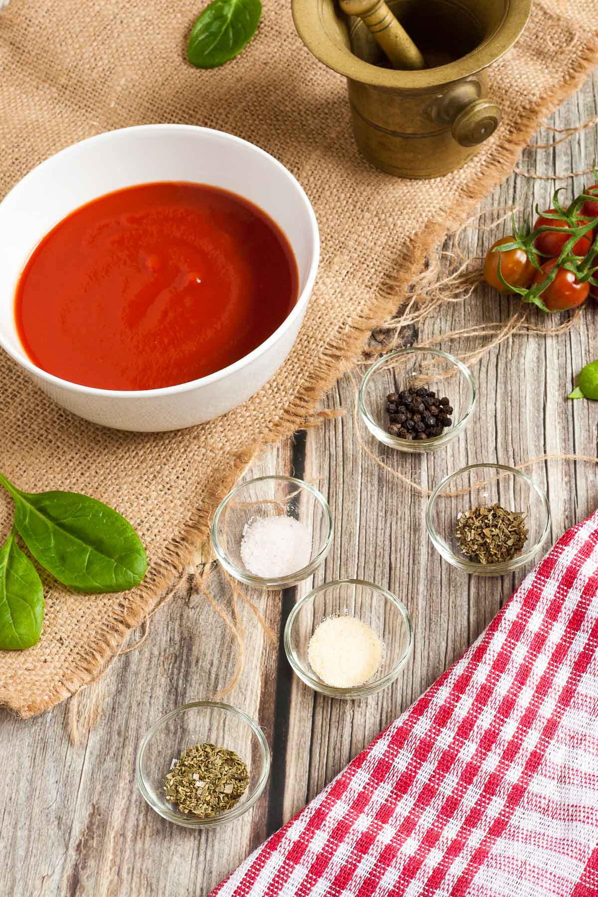 Small bowls of different ingredients to make no-cook pizza sauce like tomato sauce, oregano, basil, salt, garlic powder and pepper