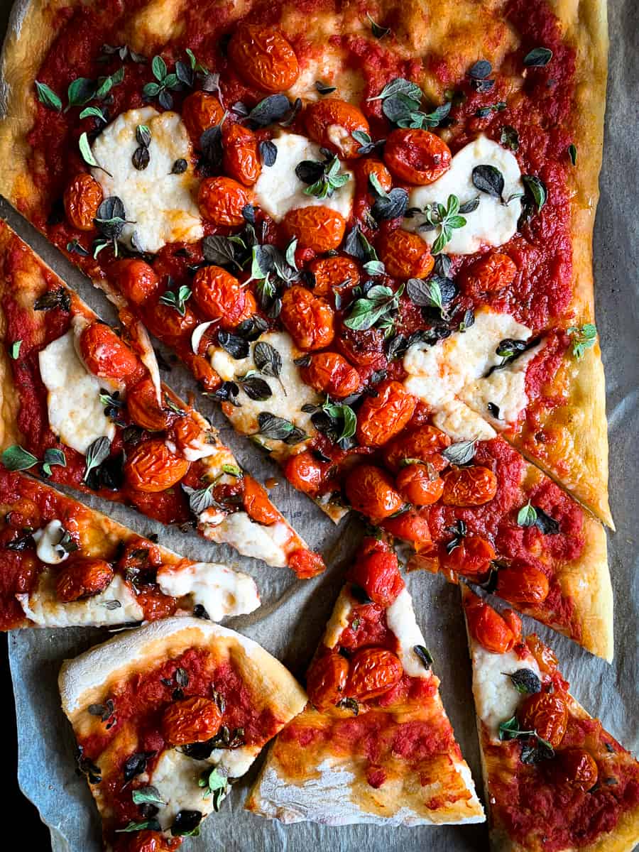 Pizza with red sauce, cherry tomatoes, melted vegan mozzarella, and fresh green herbs