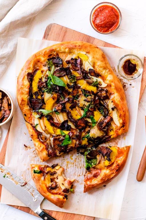 Pizza topped with butternut squash slices, dark brown bacon-like pieces and fresh chopped basil.