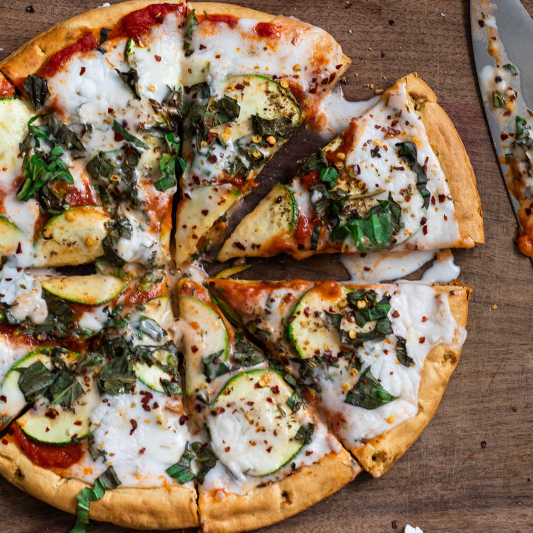 Pizza with red tomato sauce, zucchini slices, and liquid white melted mozzarella cheese. Sprinkled with chopped basil.