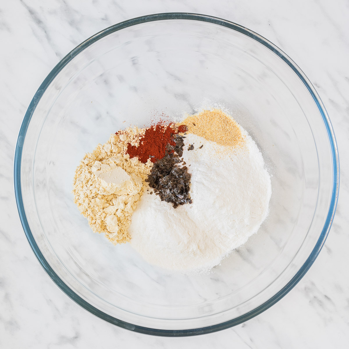 Glass bowl with flour, yellow flour, paprika powder, pepper, and yeast flakes. 