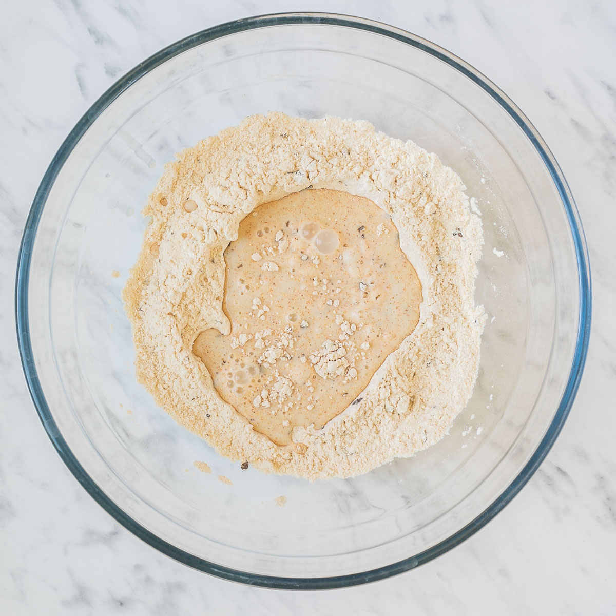 Glass bowl with light yellow flour mix and some liquid in the middle
