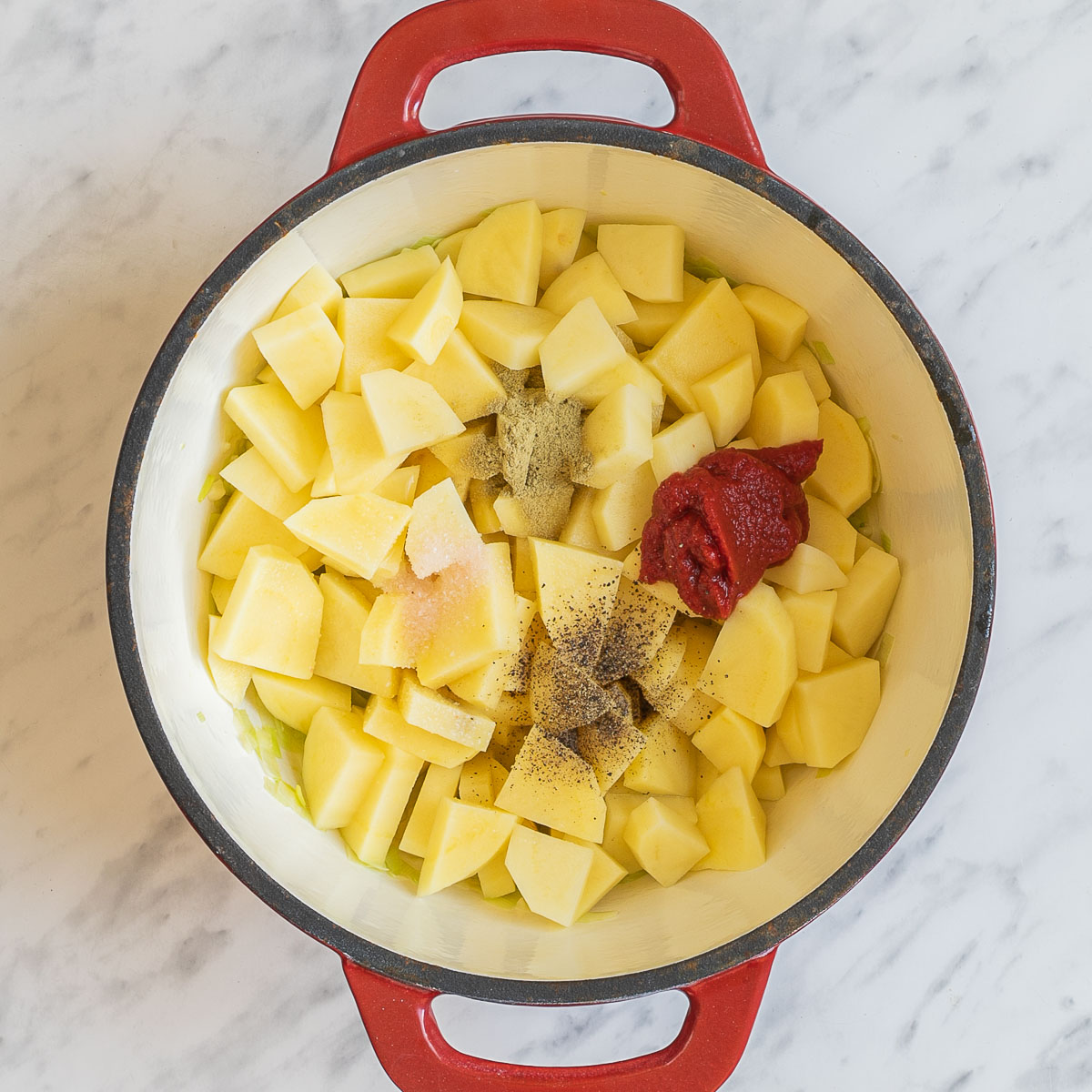 A red white enameled Dutch oven with large potato cubes and heaps of spices. 