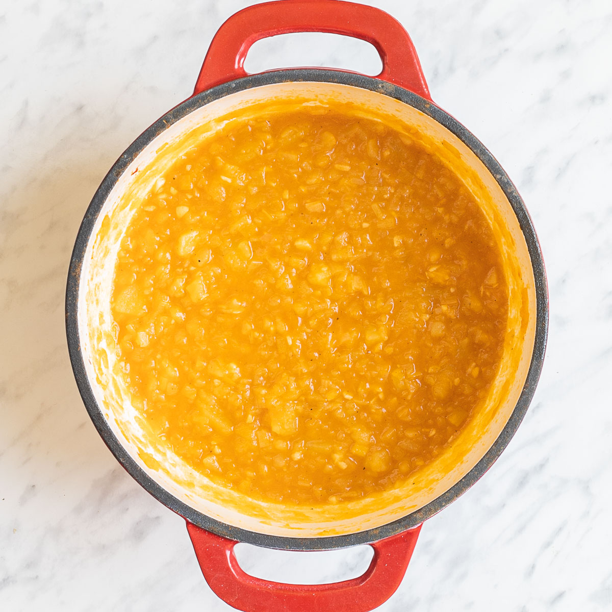 A red white enameled Dutch oven with thick stew-like orange sauce.