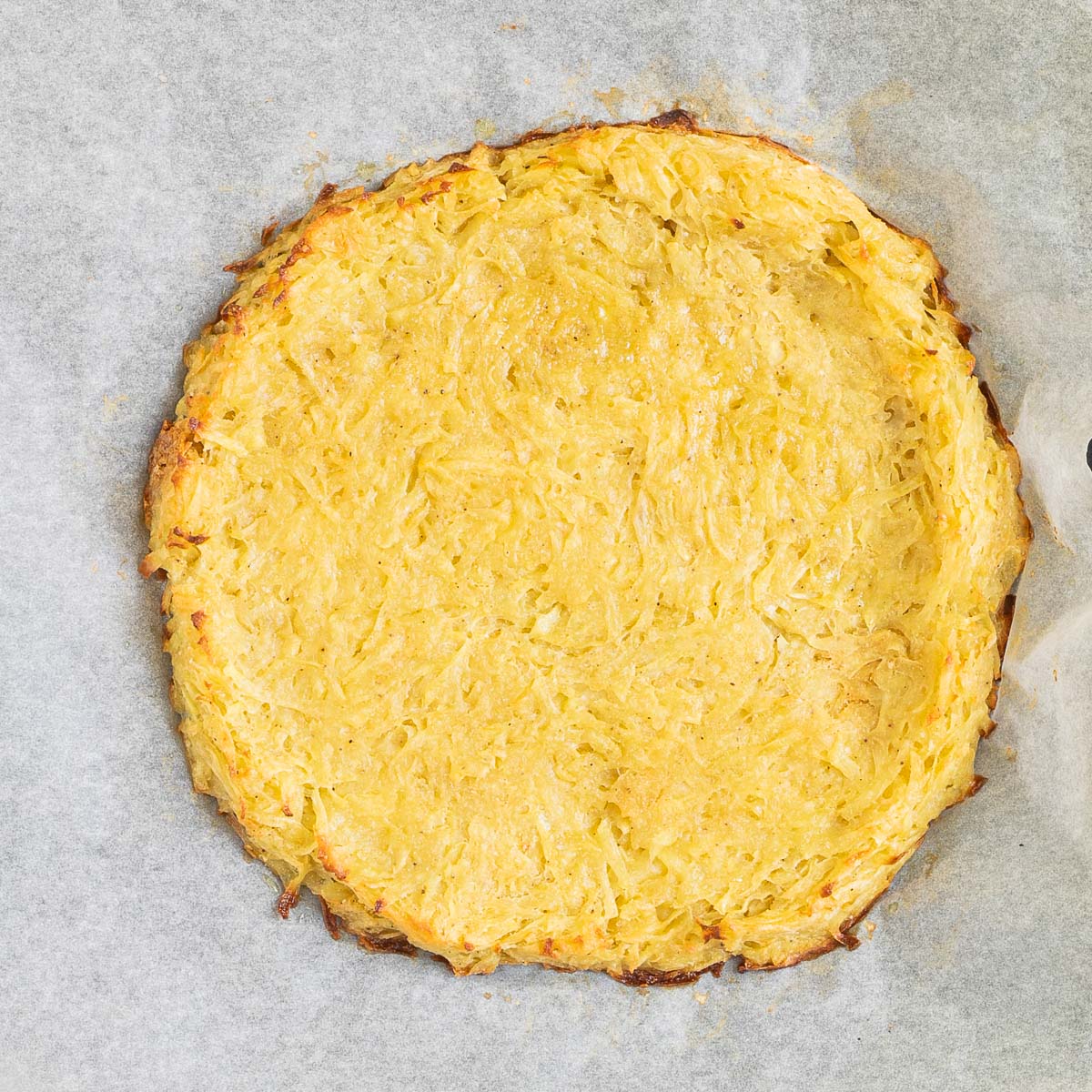 shredded potato pizza crust with slight crispy brown edges on a parchment paper.