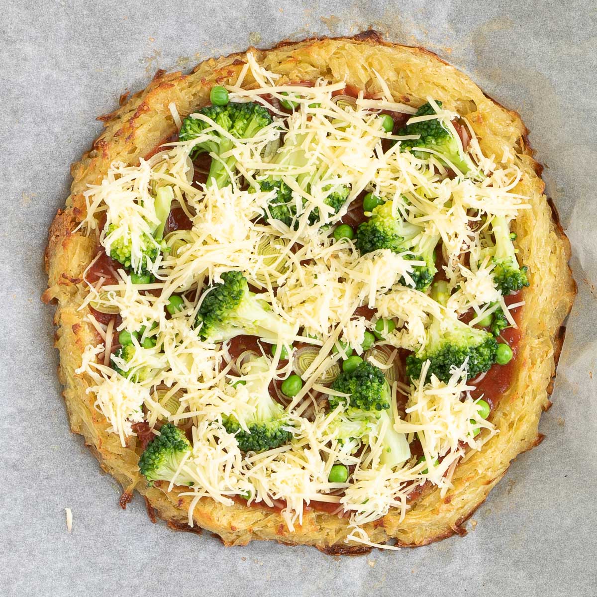 Hash brown crust pizza with topped with tomato sauce, broccoli, peas and shredded cheese.