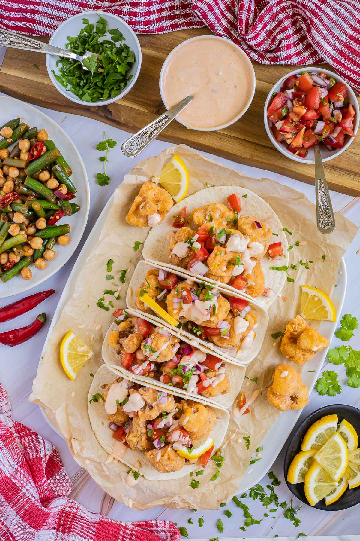 4 small tortillas folded in half on parchment paper filled with cauliflower florets, tomato, and onion pieces drizzled with a light pink sauce. Green beans, and chickpeas are served as a side.