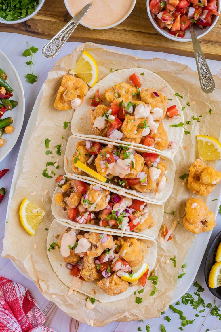 4 small tortillas folded in half on parchment paper filled with cauliflower florets, tomato, and onion pieces drizzled with a light pink sauce.