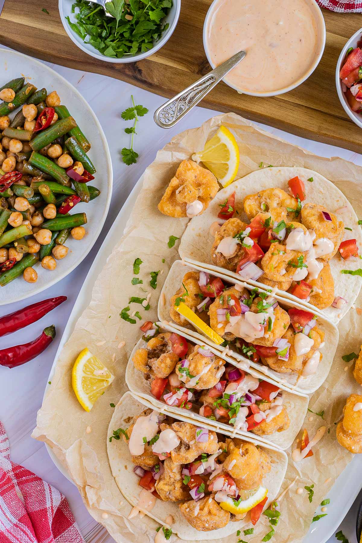 4 small tortillas folded in half on parchment paper filled with cauliflower florets, tomato, and onion pieces drizzled with a light pink sauce. Green beans, and chickpeas are served as a side.