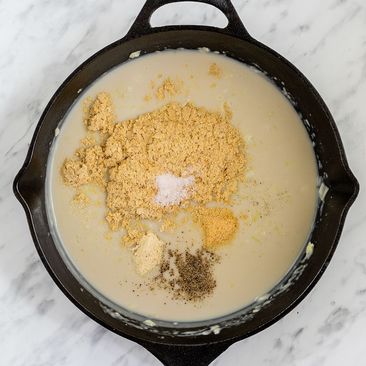 Black cast iron skillet with a light brown sauce, cheezy flakes and other spices.