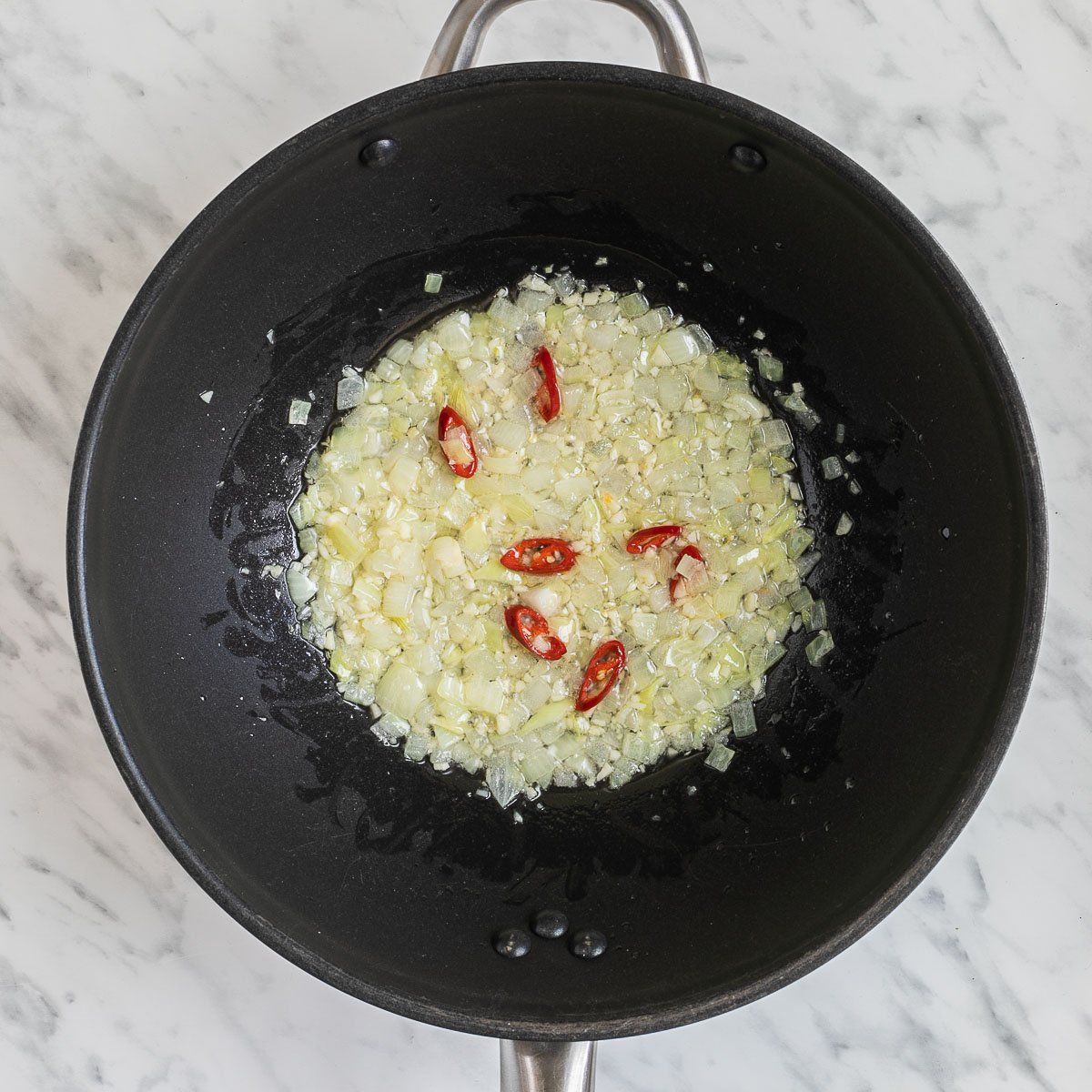 Wok with onion and chili peppers in oil.