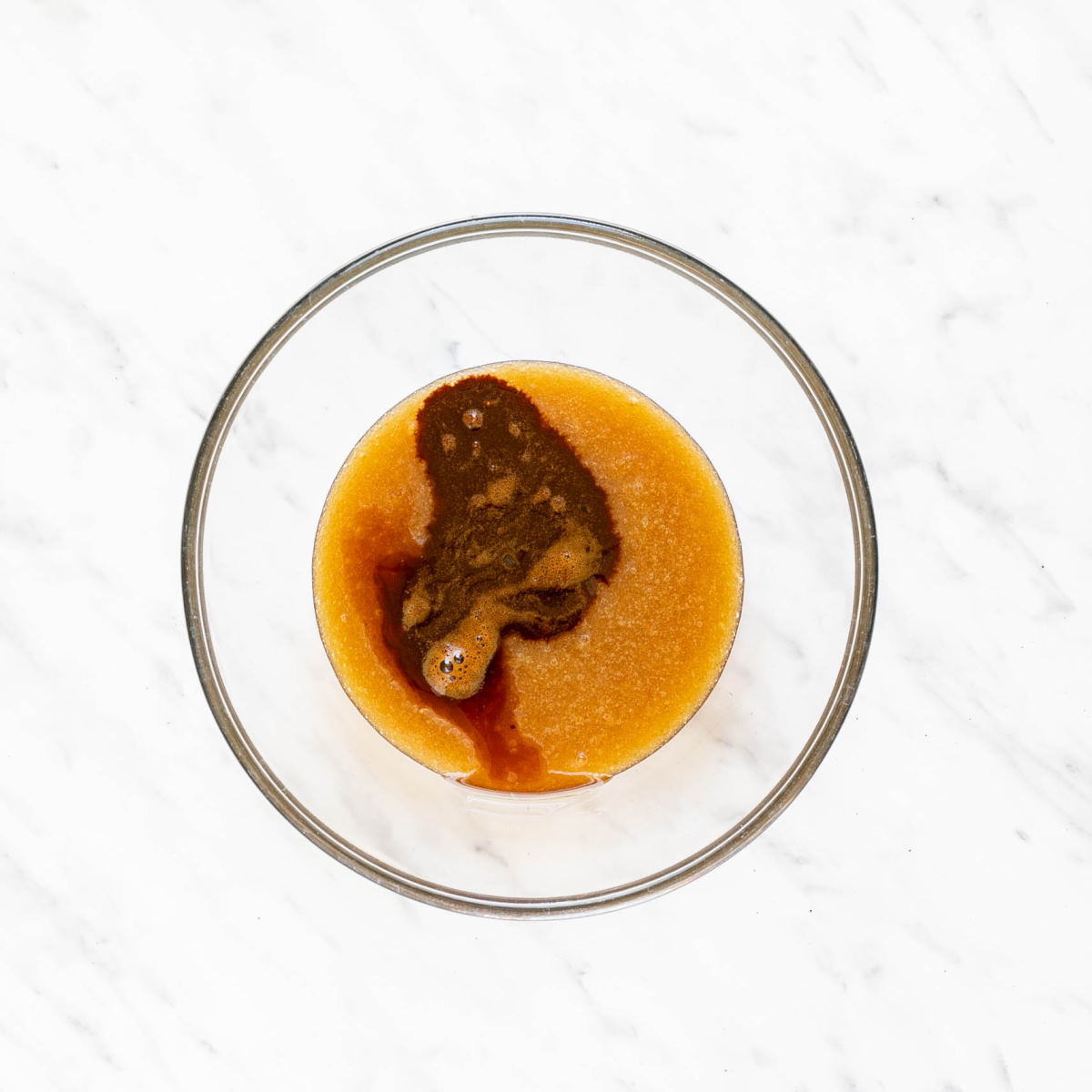 Glass bowl with caramel color liquid and a small dark brown liquid not yet mixed together.