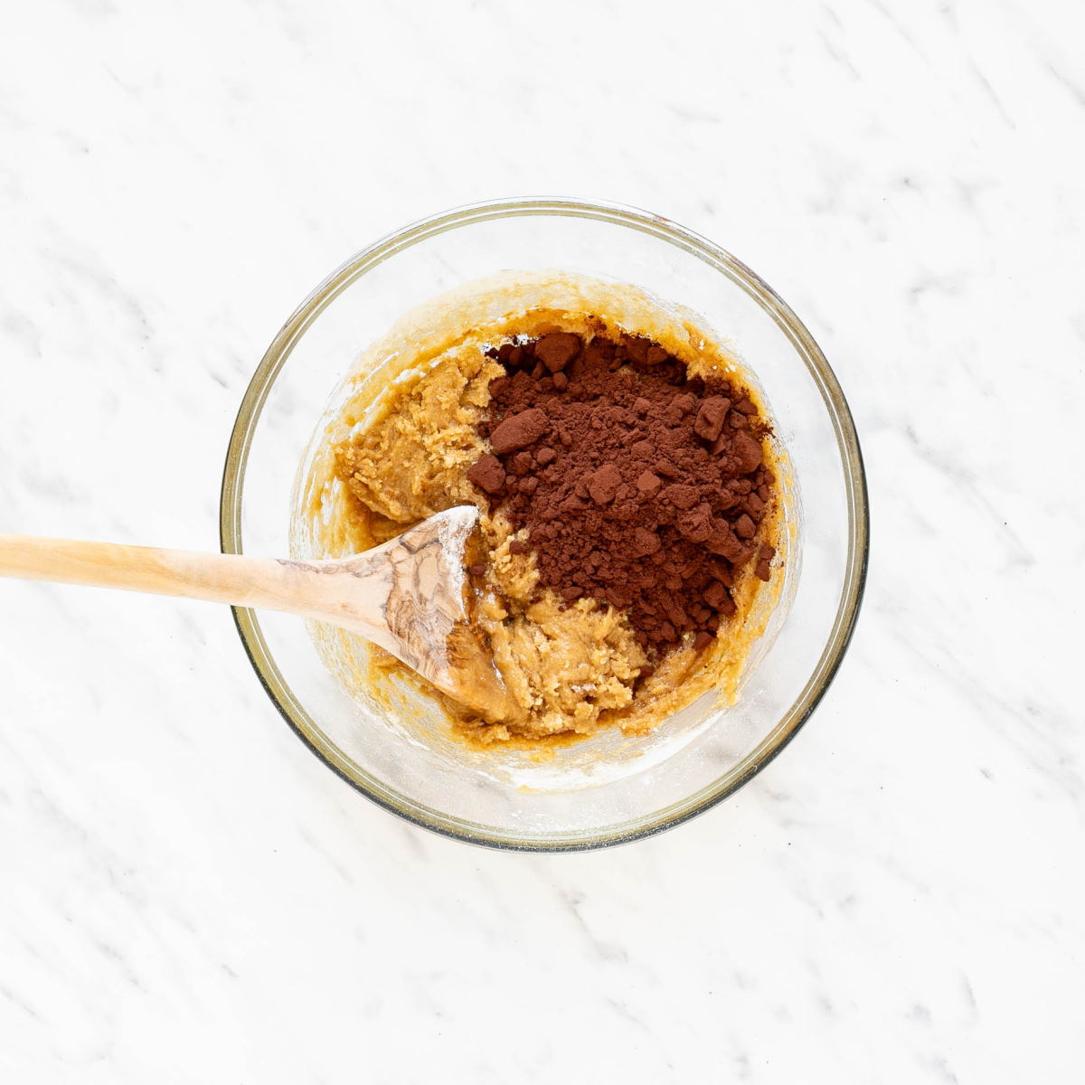 Glass bowl with brown cookie dough and cocoa powder.