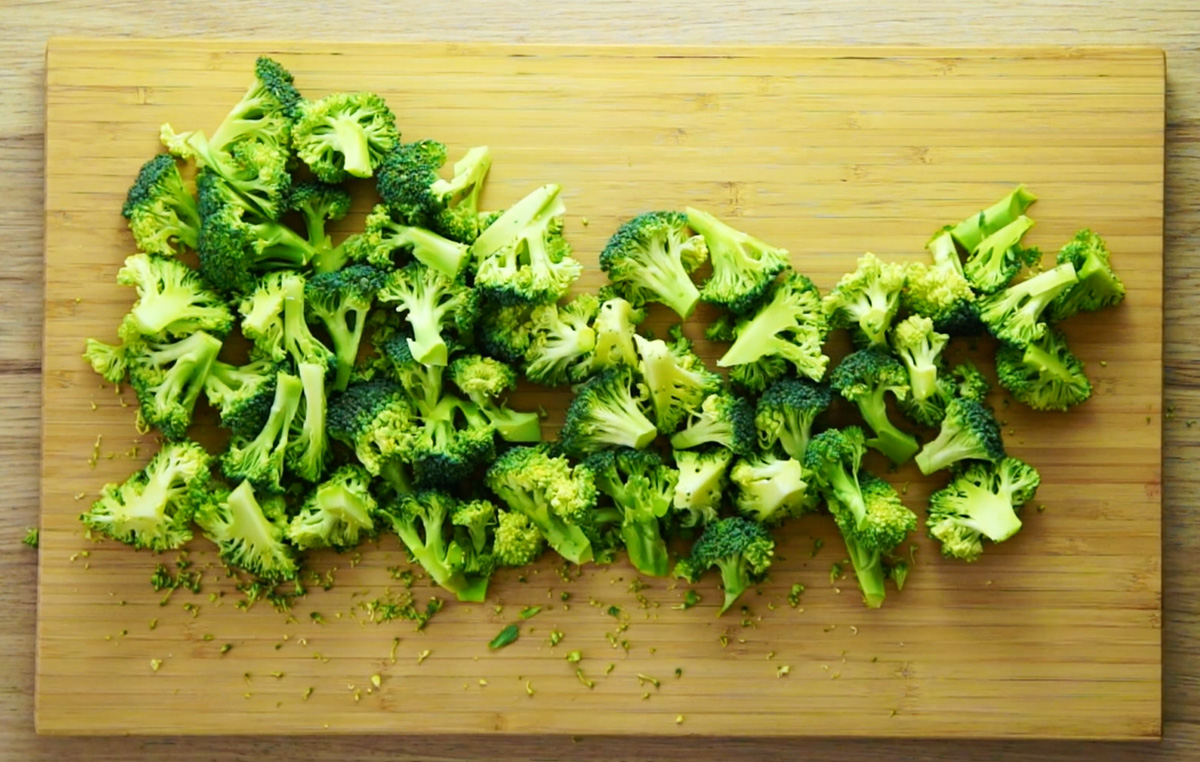 A wooden cutting board full of raw, green broccoli florets.