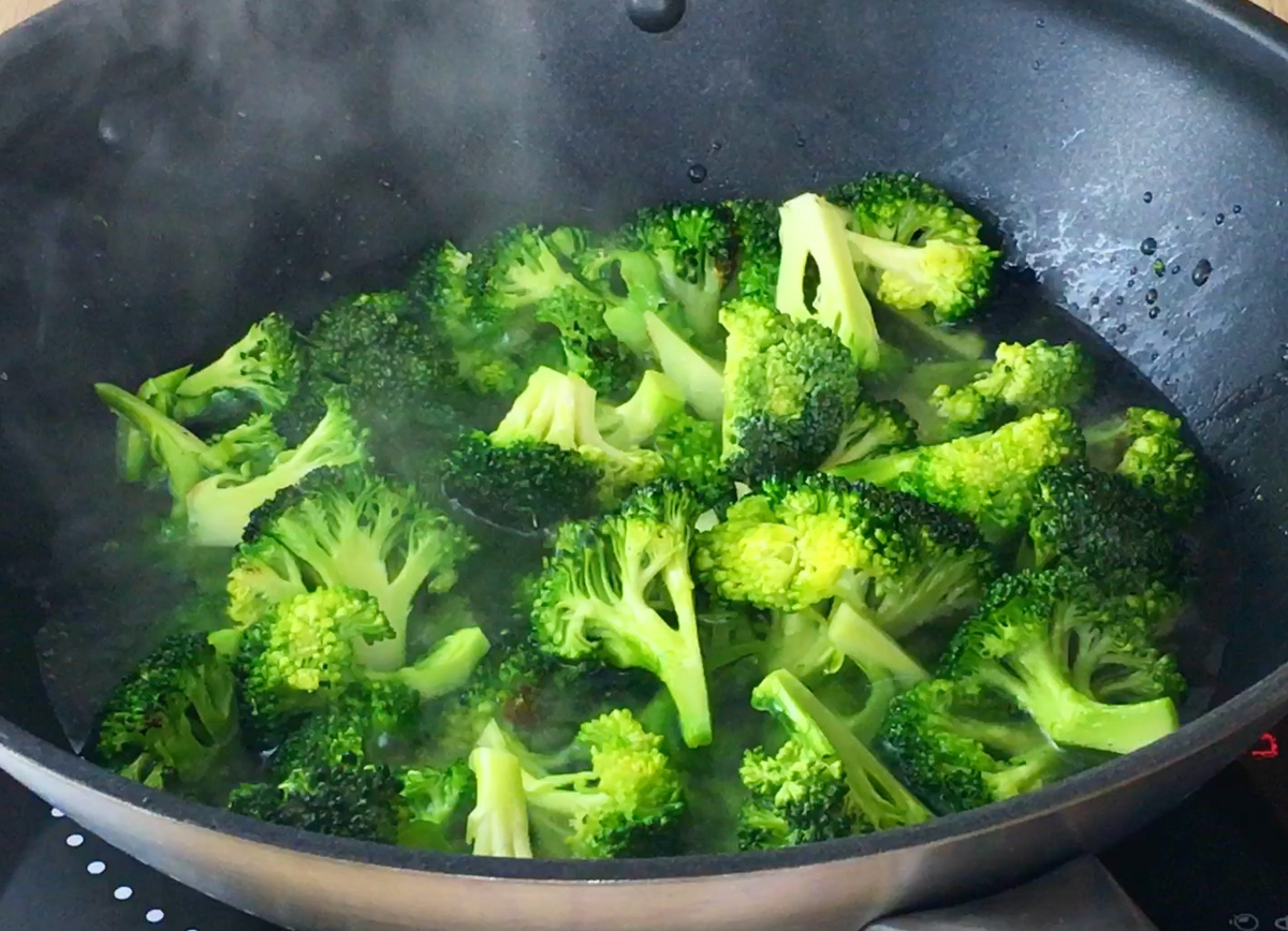 A wok half filled with water and green broccoli florets.