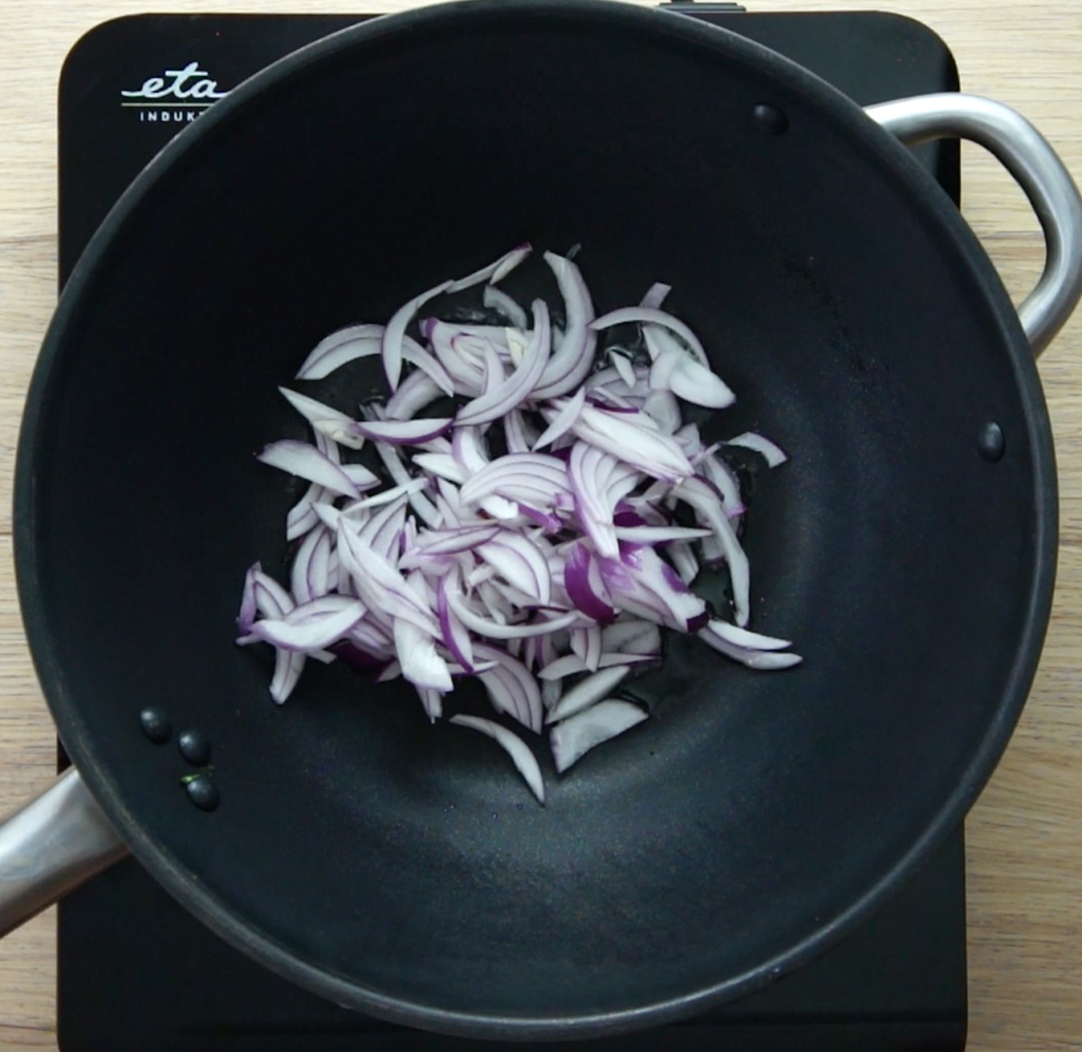 A wok with several red onion slices.