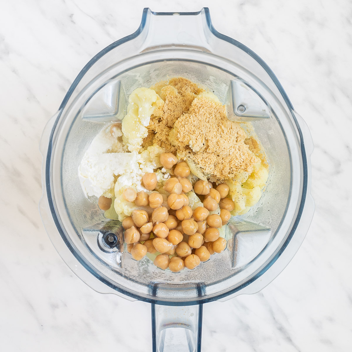 Blender from above with cauliflower florets chickpeas, starch, and flakes.