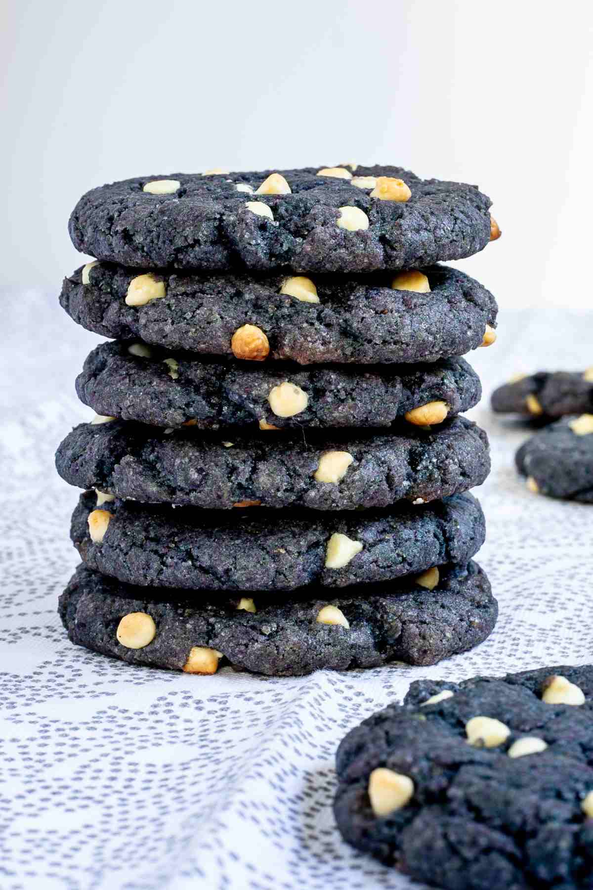 A stack of blue-purple cookies with white chocolate chips on a white-grey surface.