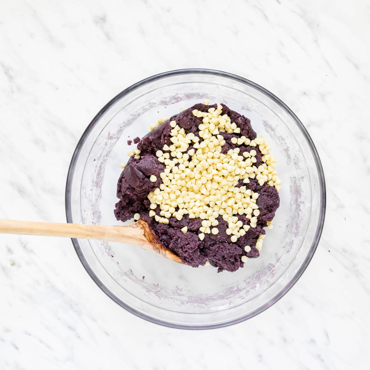 A glass bowl with a raw purple cookie down and white chocolate chips. 