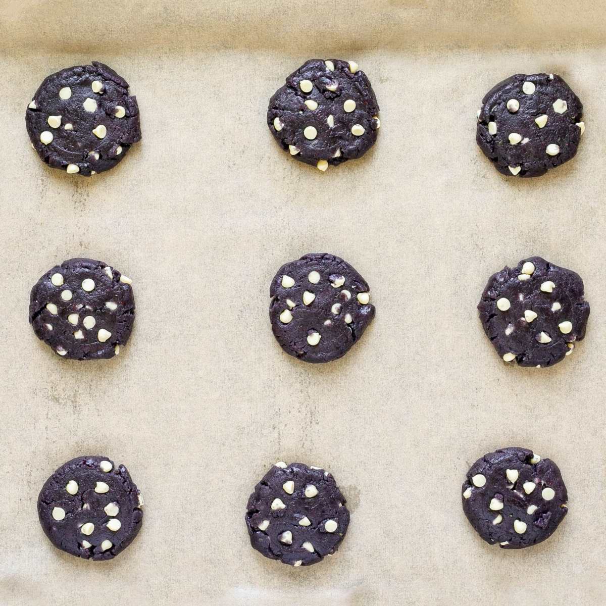 Raw purple cookies with white chocolate chips on parchment paper. 