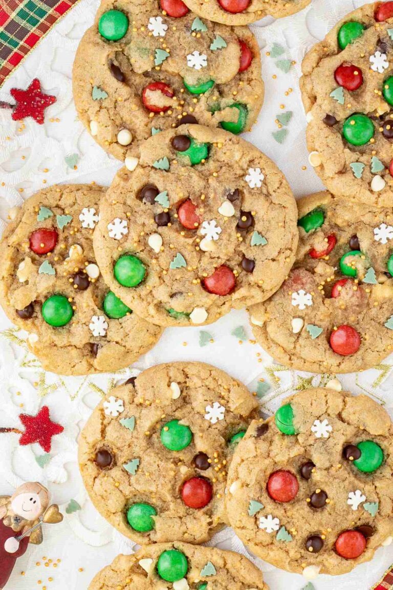 Light brown cookies with red and green m&ms, chocolate chips, tiny white sugar snowflakes, and tiny green pine trees.