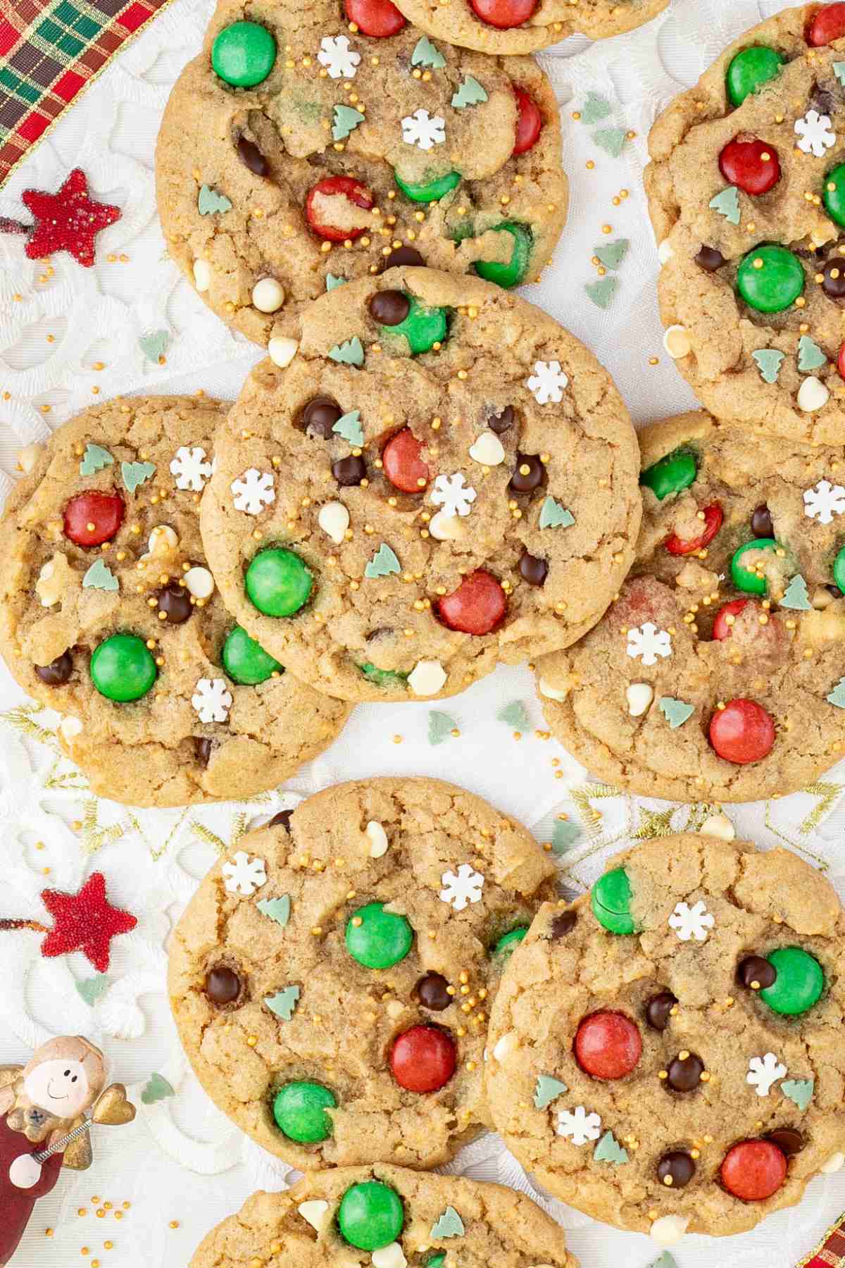 Light brown cookies with red and green m&ms, chocolate chips, tiny white sugar snowflakes, and tiny green pine trees.